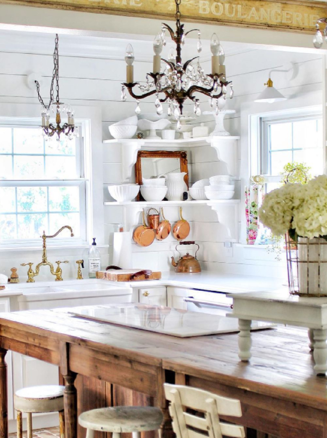 Charming old brass chandeliers, wood toned island, and white French country details in a glorious kitchen (Simply French Market). #frenchkitchen #europeancountrystyle