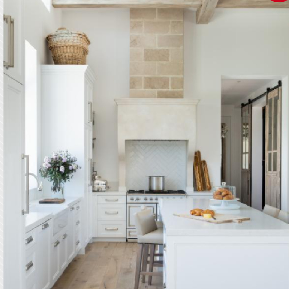 Pale tones and serenity in a sophisticated white European country kitchen with high ceilings, farm sink, and warm stone - The Refined Group.