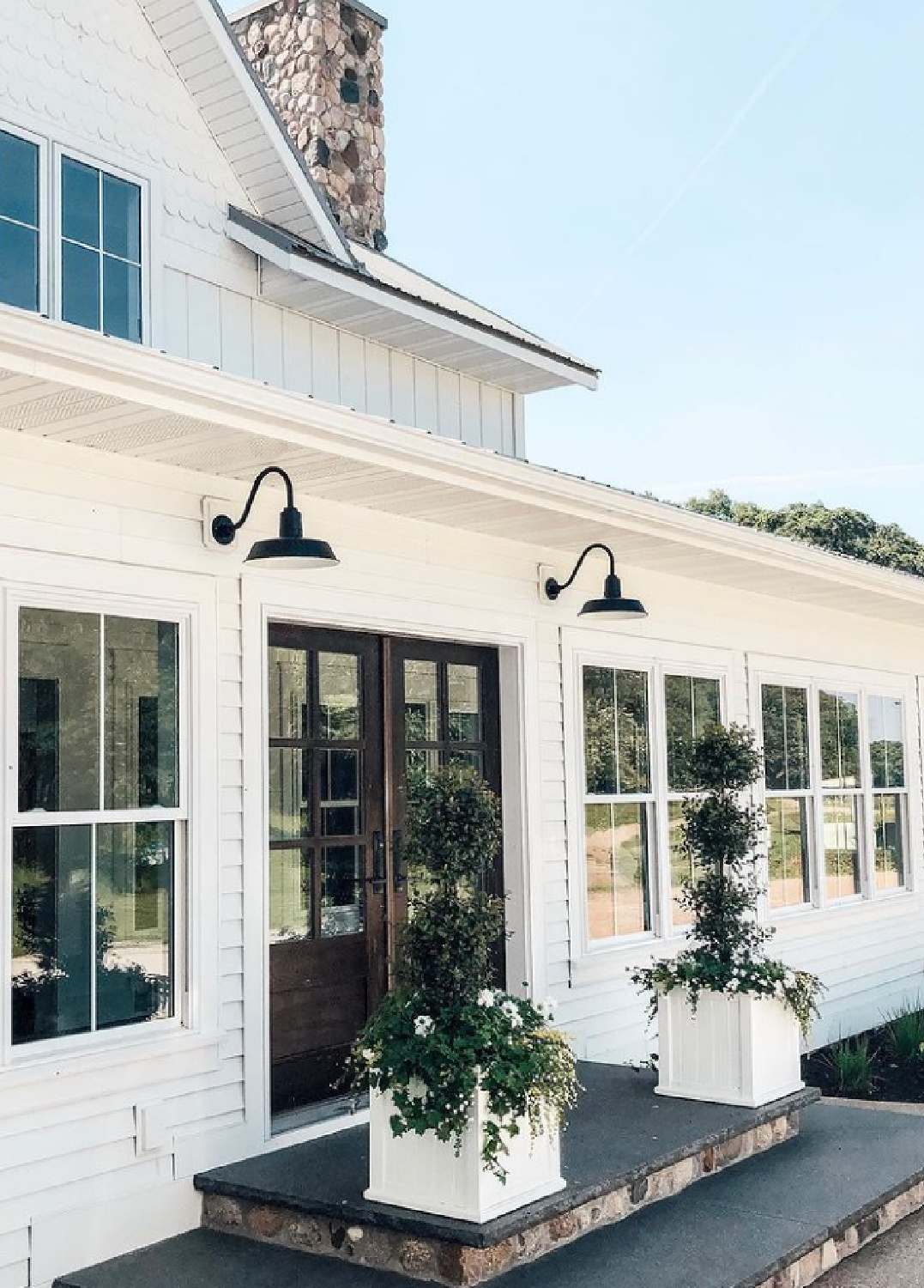 SW Pure White paint color on a beautiful farmhouse with black doors and topiaries on porch - @balance_and_bison. #swpurewhite #whitepaintcolors #houseexteriorpaint