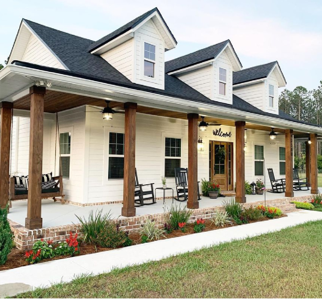 SW Pure White paint color on farmhouse exterior with dormers and wood supports on wrap around porch - @gregoryfarmhouse. #swpurewhite #whitepaintcolors #whitehousecolors