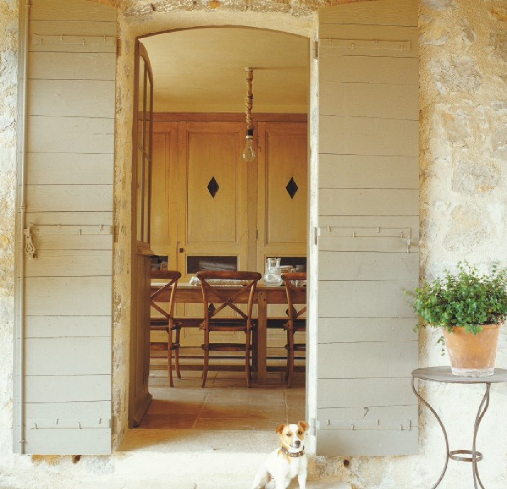French farmhouse entrance with beautiful tall muted grey shutters and little French dog - from La Vie Est Belle (Henrietta Heald/Ryland Peters Small). #frenchfarmhouse #frenchkitchen #frenchshutters #frenchdog