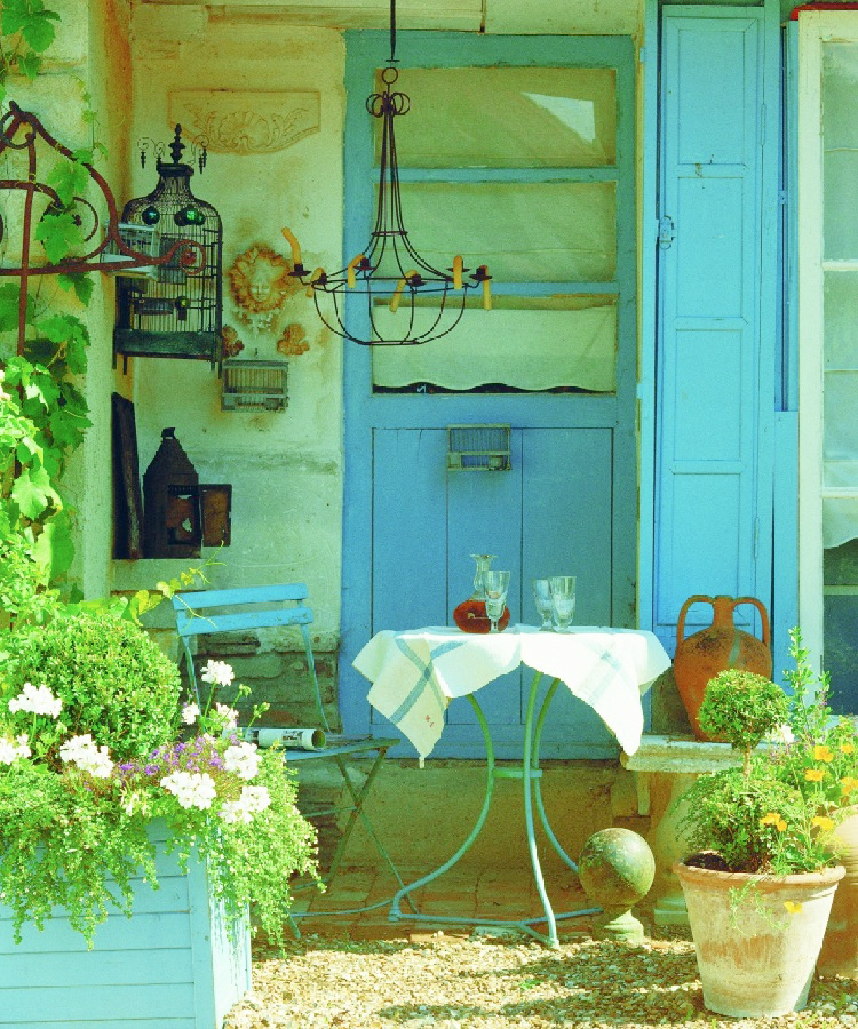 Bright blue shutters and accents in French farmhouse garden with bistro chair - from La Vie Est Belle by Henrietta Heald. #frenchgarden #frenchcountryexterior #frenchhomes