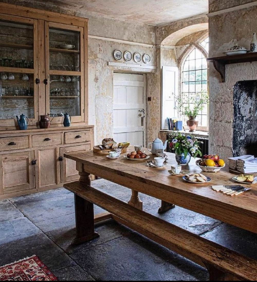 Beautiful rustic European country kitchen with long farm table and bench, stone, and gothic window - @dursladefarmhouse. #europeancountry #europeankitchen #rustickitchens
