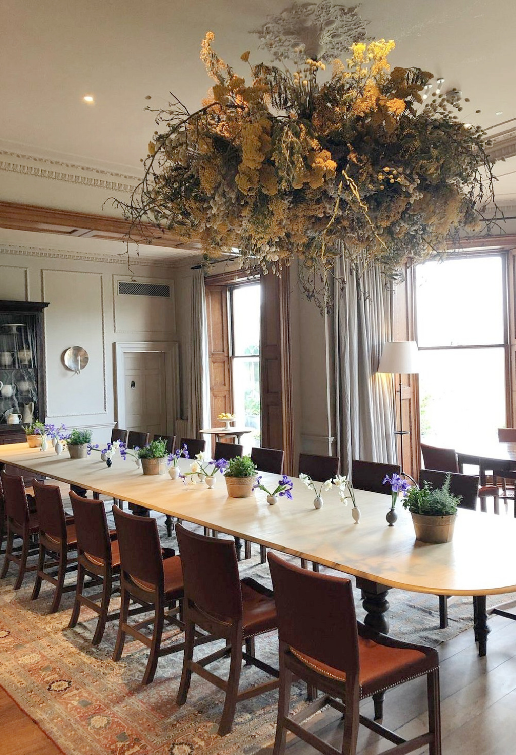 Fanciful dried floral chandelier above long oval dining table at Heckfield Place in Hampshire England. #hotels #heckfieldplace