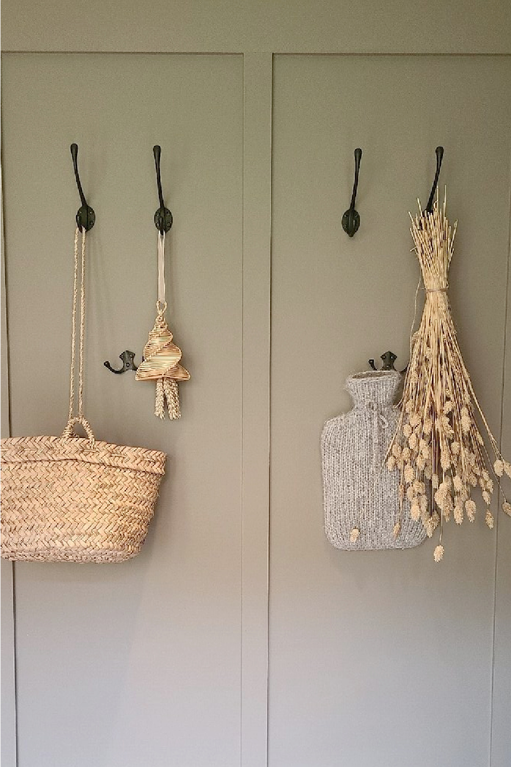 English country style board and batten moulding and hooks with natural woven basket, corn dolly, and hot water bottle at Heckfield Place in Hampshire, England.