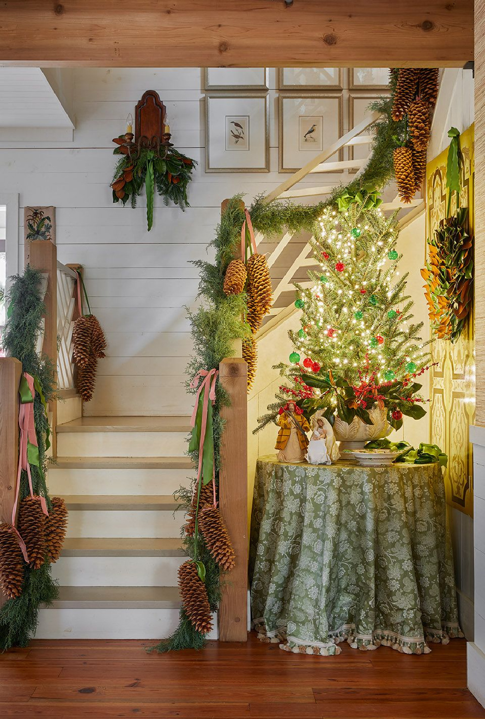 Breathtaking holiday staircase decorated with garland and small Christmas tree on skirted round table in James Farmer's charming home - from CELEBRATING HOME (Gibbs Smith, 2022). #holidaydecor #staircase