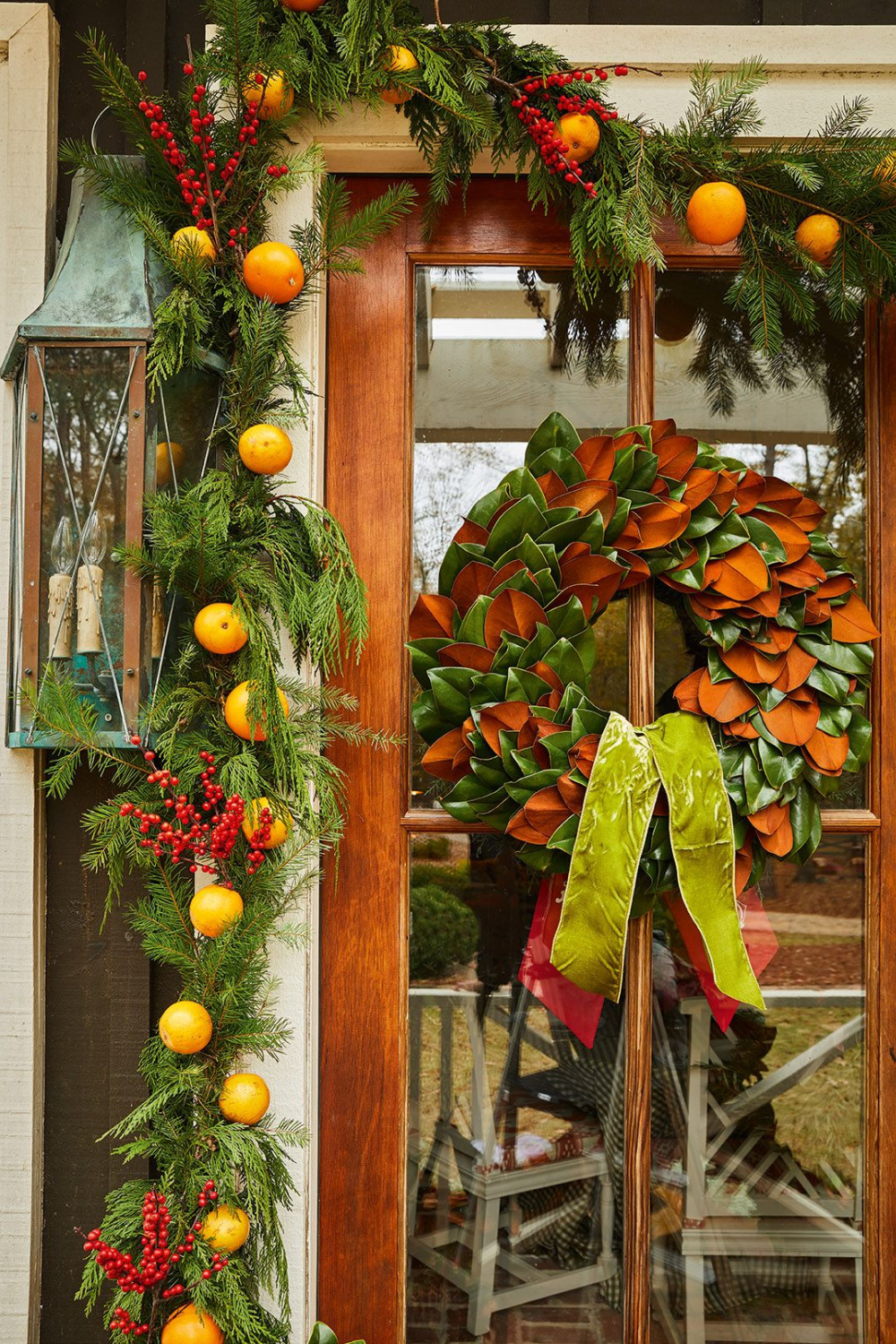 Beautiful magnolia leaf holiday wreath with ribbon and citrus garland adorning door - from CELEBRATING HOME (Gibbs Smith, 2022). #magnoliawreath #christmaswreaths
