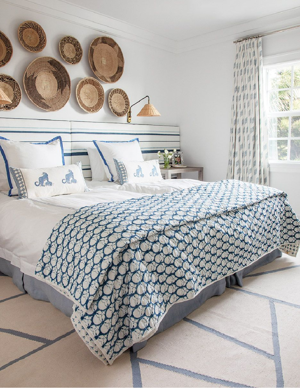 Handwoven baskets from Zimbabwe and wicker sconce above bed with indigo striped headboard and bedding - design by Anne Hepfer in MOOD (Gibbs Smith, 2022). #blueandwhite #beachybedroom
