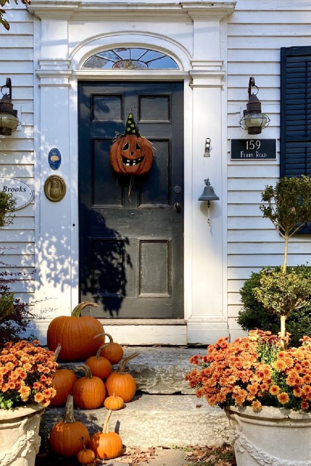 Warm orange pumpkins and mums at a farmhouse front door with vintage Jack-o-lantern - Nora Murphy.