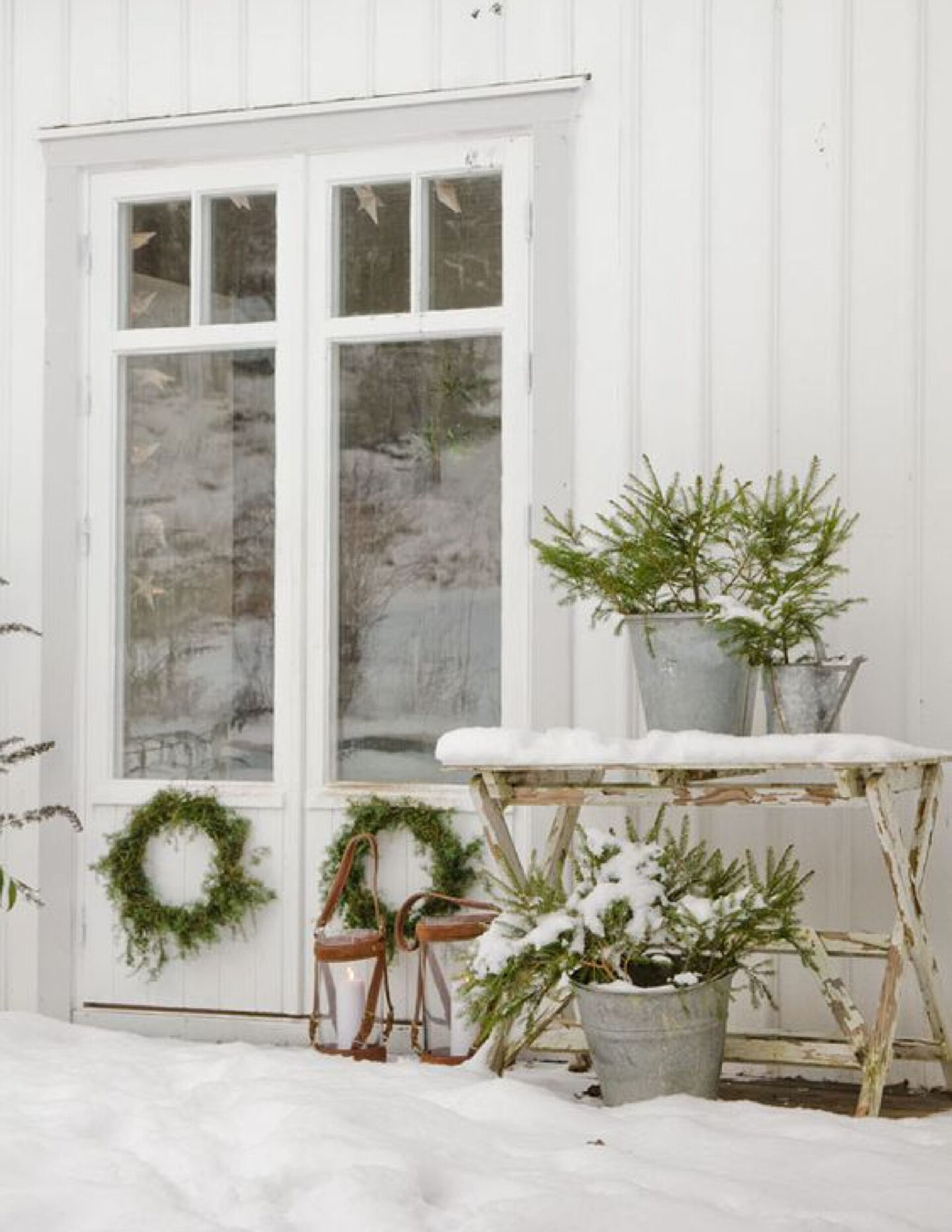 Board and batten white Scandi cottage decorated for Christmas with fresh natural greenery via Planete-Deco.