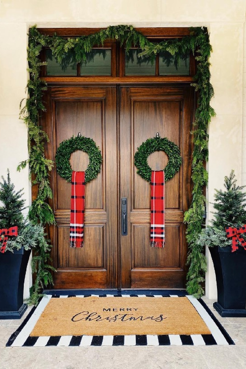 Classic Christmas holiday porch with wreths, plaid, layered doormat and tall planters - @a.woman.like.you