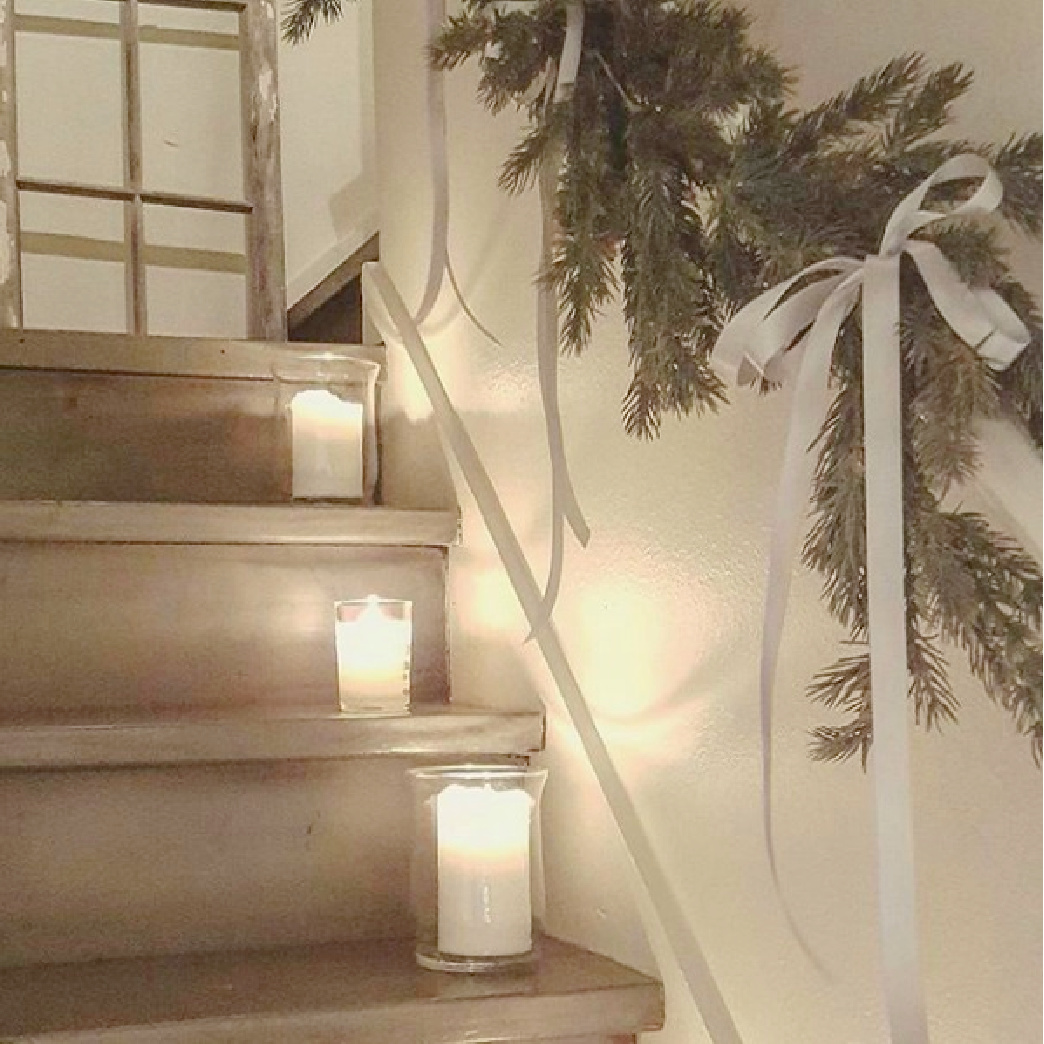 Pretty French country Christmas decor in a staircase with candles, fresh greenery, and white ribbon - The French Nest Co Interior Design.