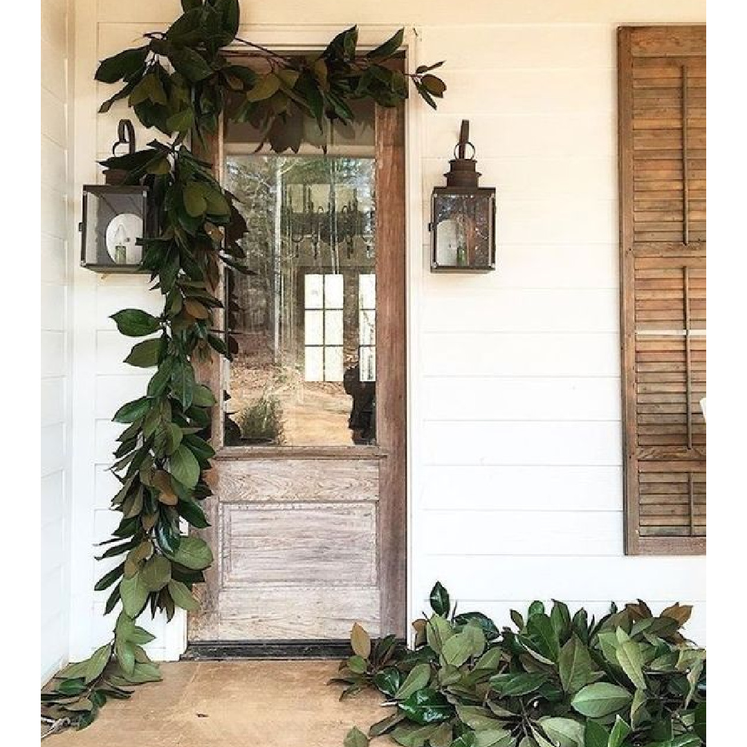 Christmas garland swagged on front door with lanterns flanking - McGee Studio. #modernfarmhouse #christmasgreenery #frontporch