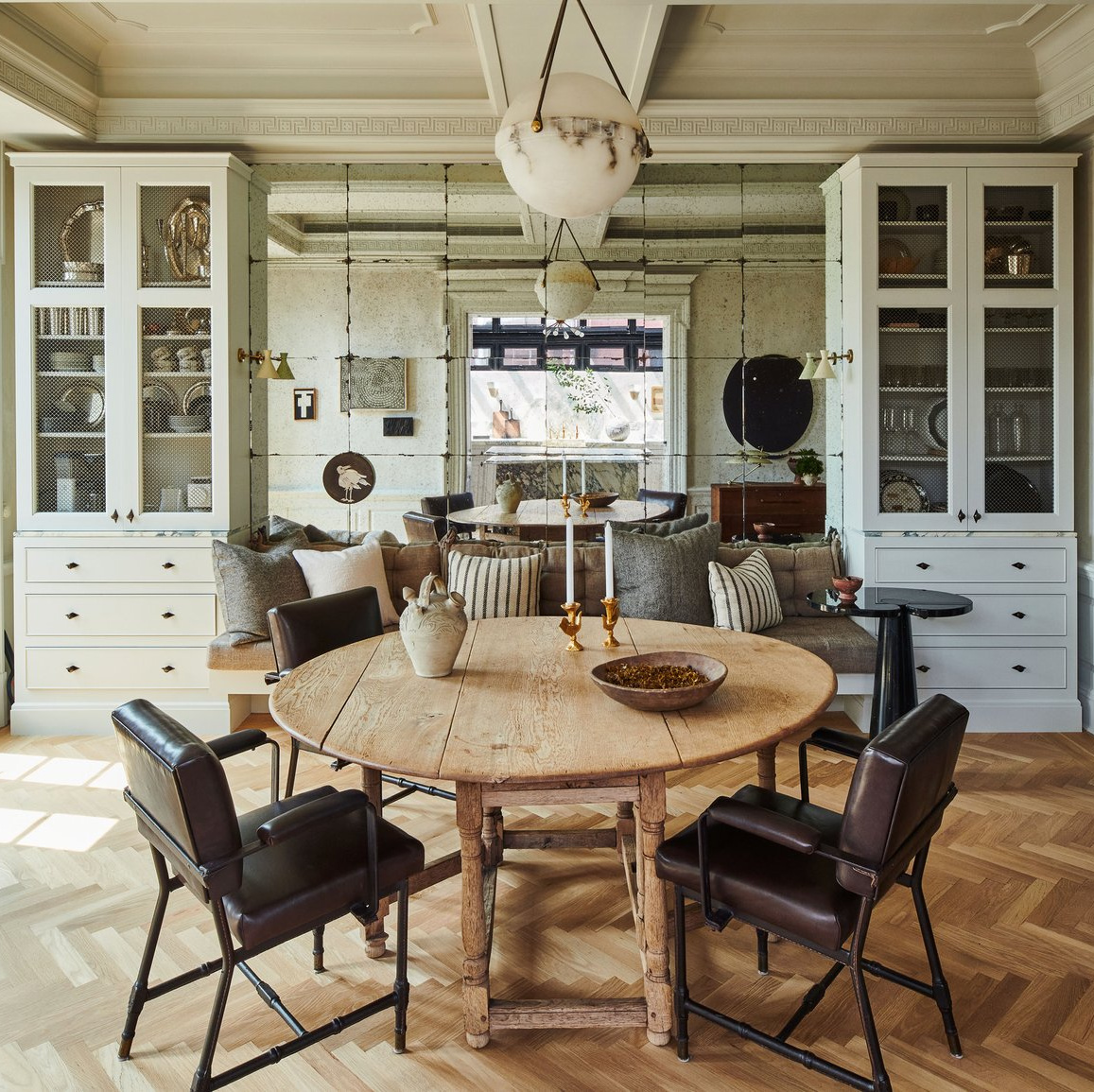 Chic dining room in Nate Berkus and Jeremiah Brent's NYC townhouse with antiques, antiqued mirror with banquiette and reflection of kitchen - AD.
