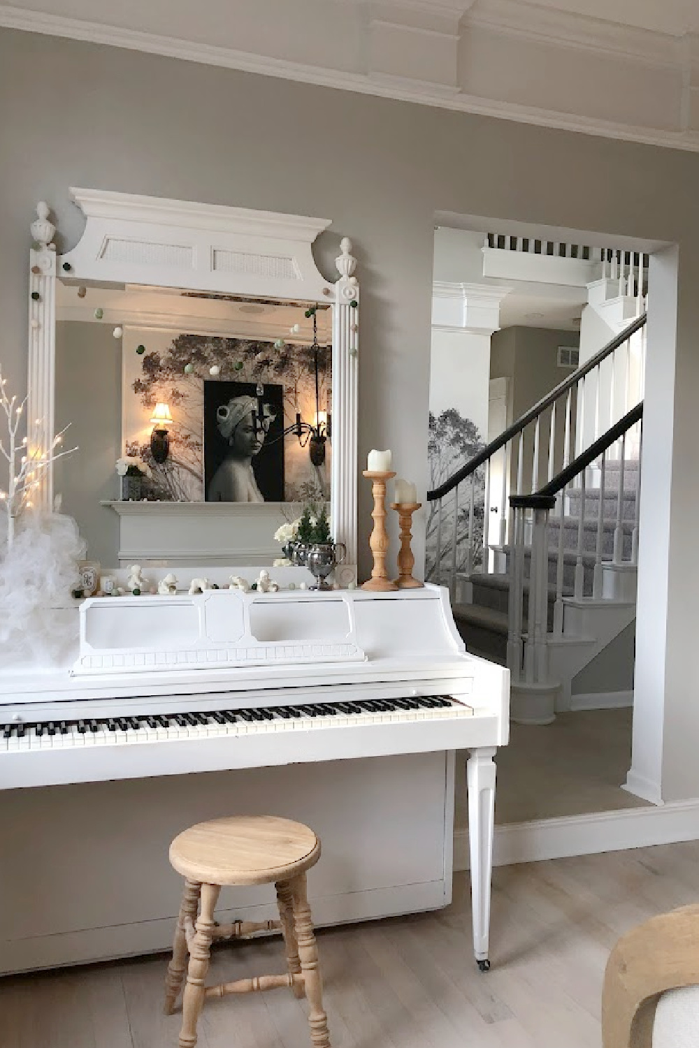 Our dining room with fireplace is used as a music room where a white piano and antique mirror are decorated for Christmas in white - Hello Lovely Studio. #whitechristmas #whitepiano