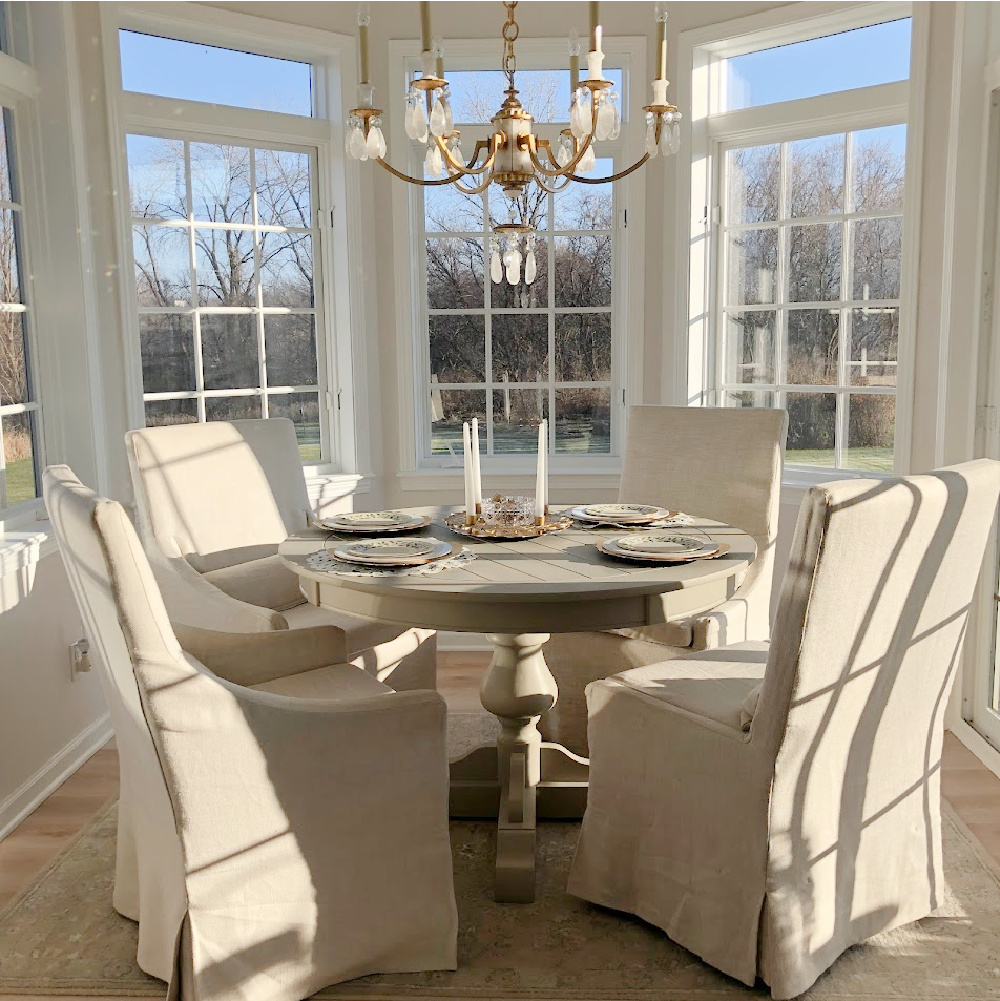 Linen slipcovered dining chairs and stone color pedestal table with Elizabeth chandelier (Thomas O'Brien) in breakfast room - Hello Lovely Studio. #elizabethchandelier #gildedchandelier #breakfastnook