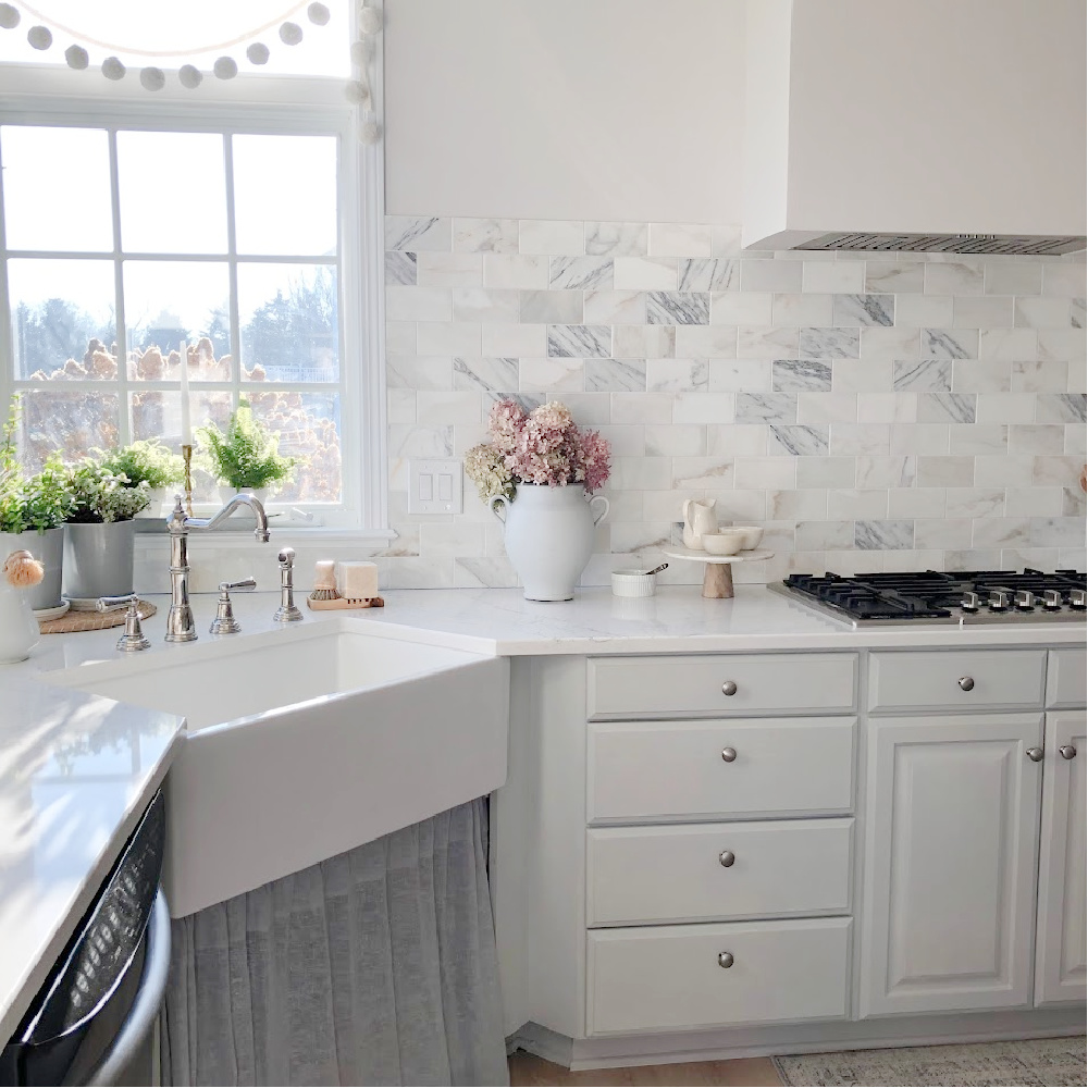 Pom pom garland at the kitchen sink window - Hello Lovely Studio. #paviliongray #graykitchen #calacattagoldmarble