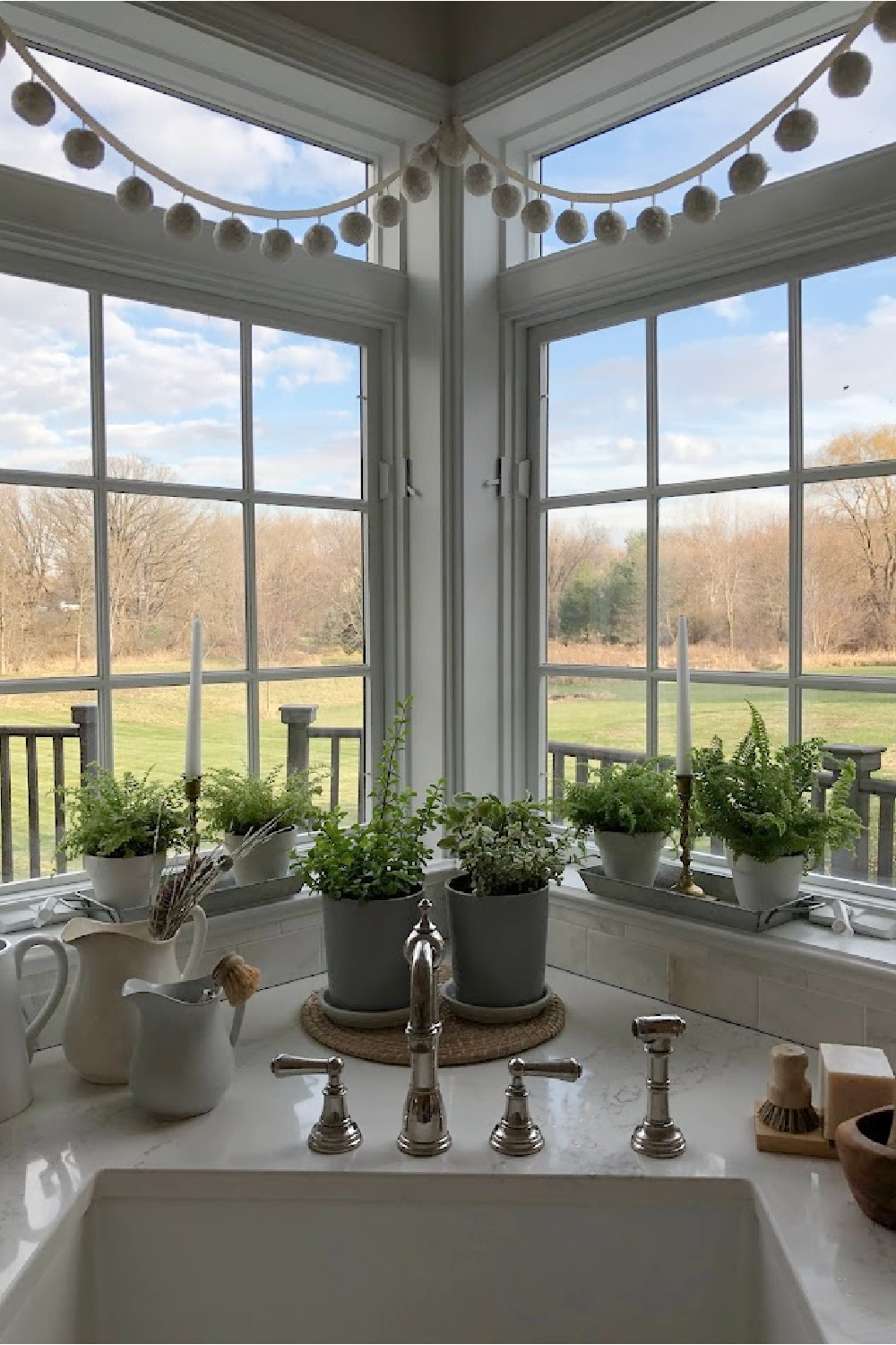 Ferns and succulents in the pom pom garland swagged windows near our farm sink. The faucet is Perrin & Rowe Edwardian Double Handle - Hello Lovely Studio.