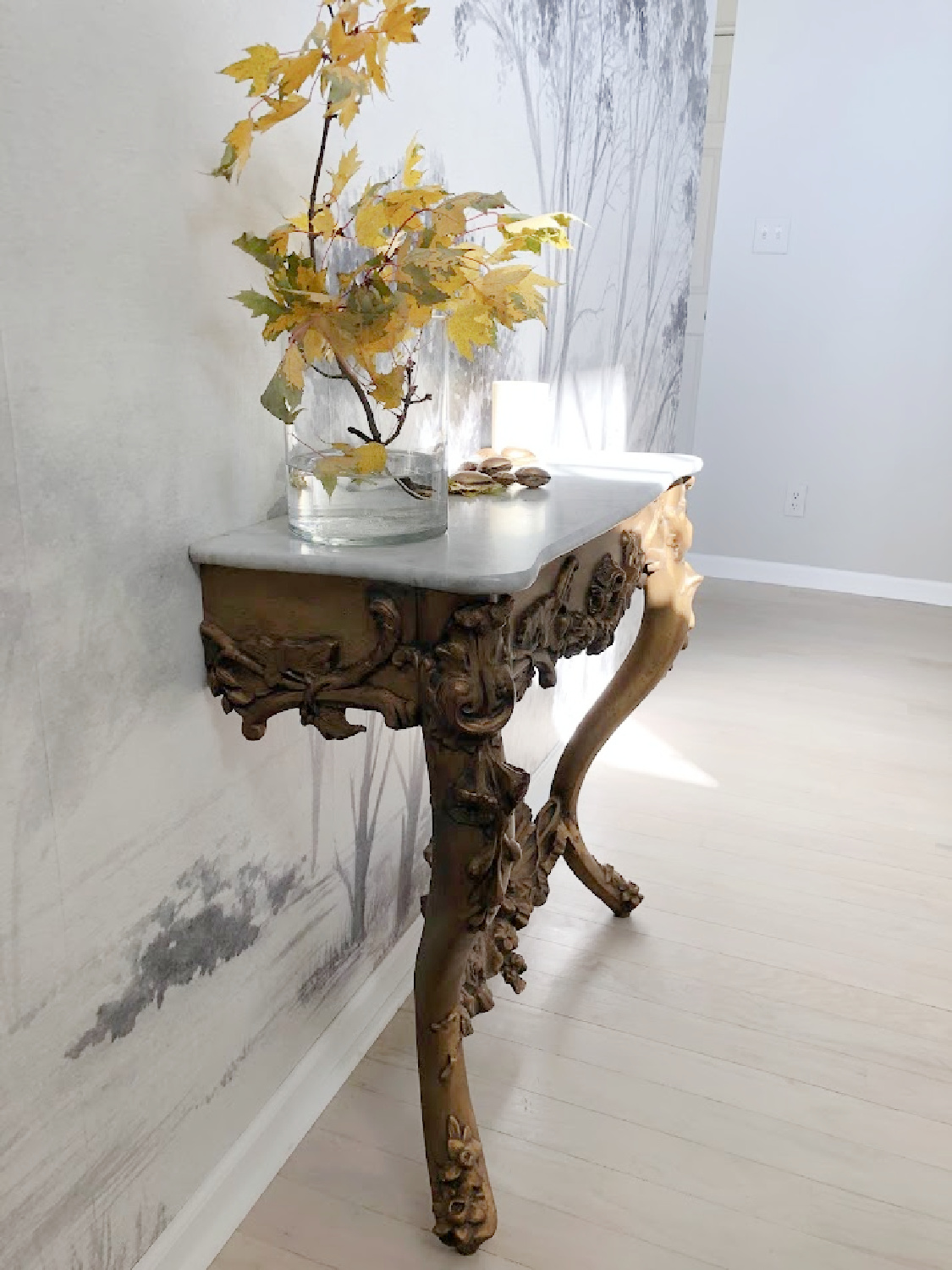 Antique French console with marble top in renovated entry with tree wallpaper mural - Hello Lovely Studio.