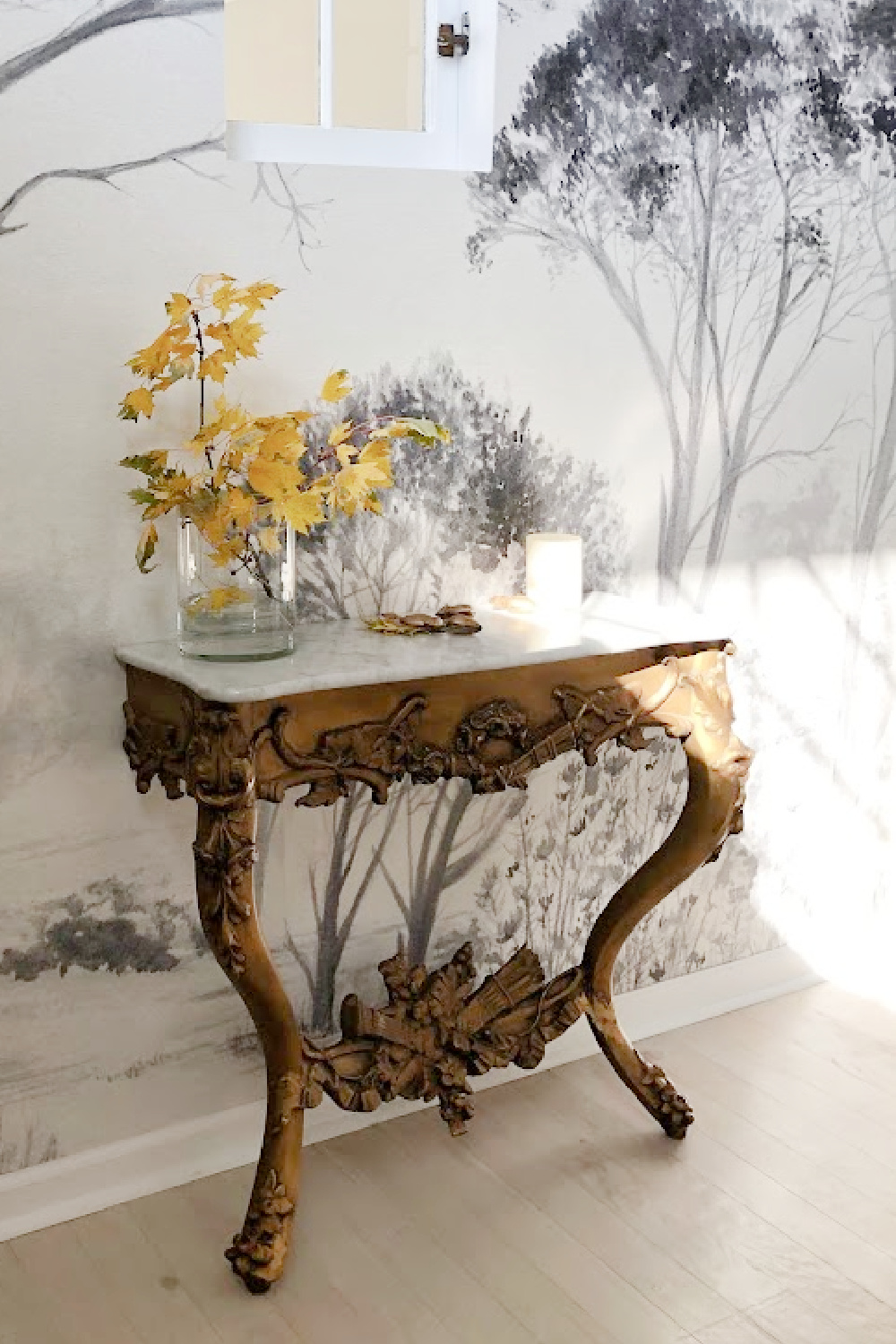 Antique French console with marble top in renovated entry with tree wallpaper mural - Hello Lovely Studio.