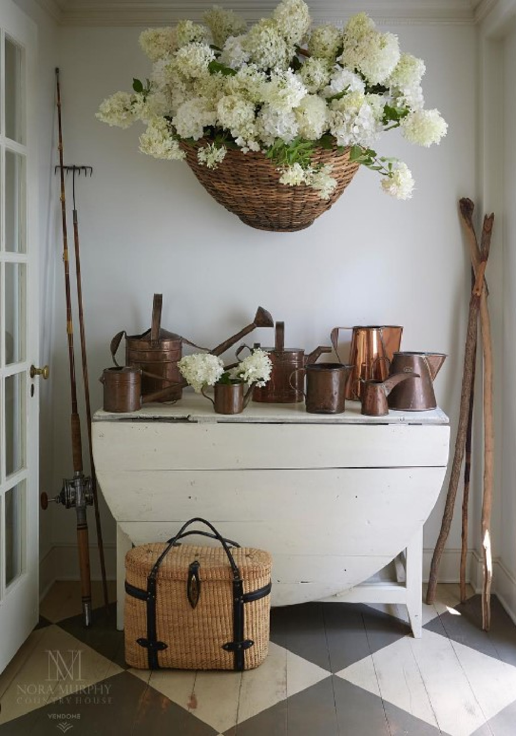 Checkered wood floors in Nora Murphy's country house - large basket of hydrangea hangs on wall above a drop leaf table. #checkeredfloors #americancountrystyle #americanfarmhouse