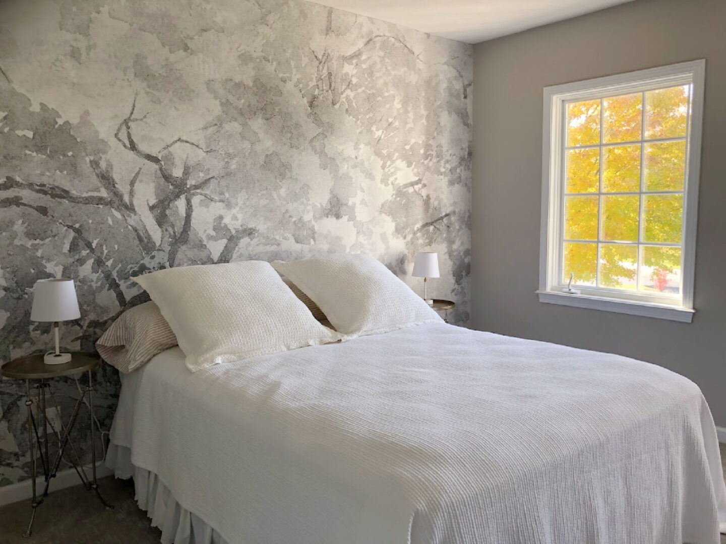 Guest bedroom with grisaille wallpaper mural and gold maple tree through window.