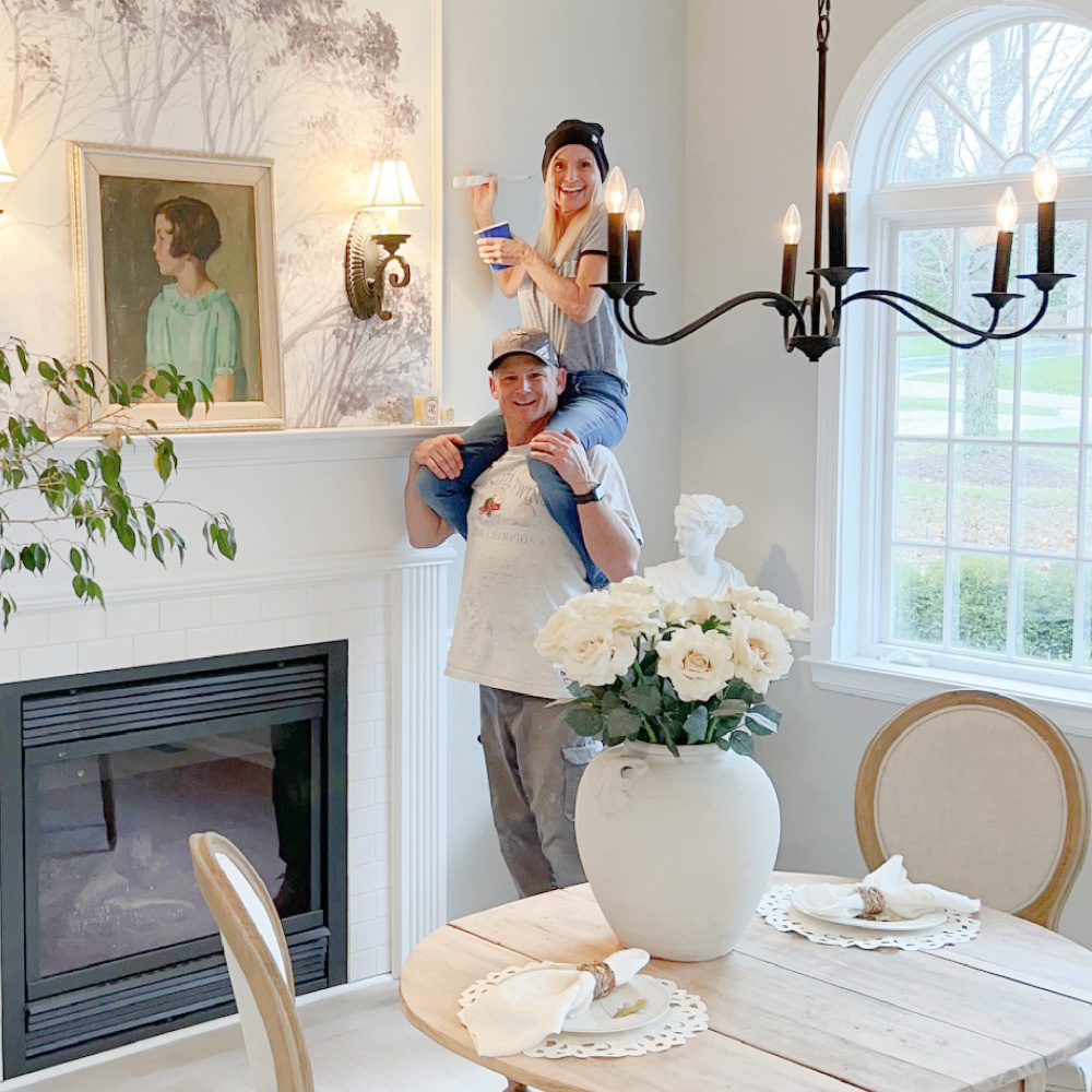 Michele on husband's shoulders painting in dining room with mural over fireplace - Hello Lovely Studio.