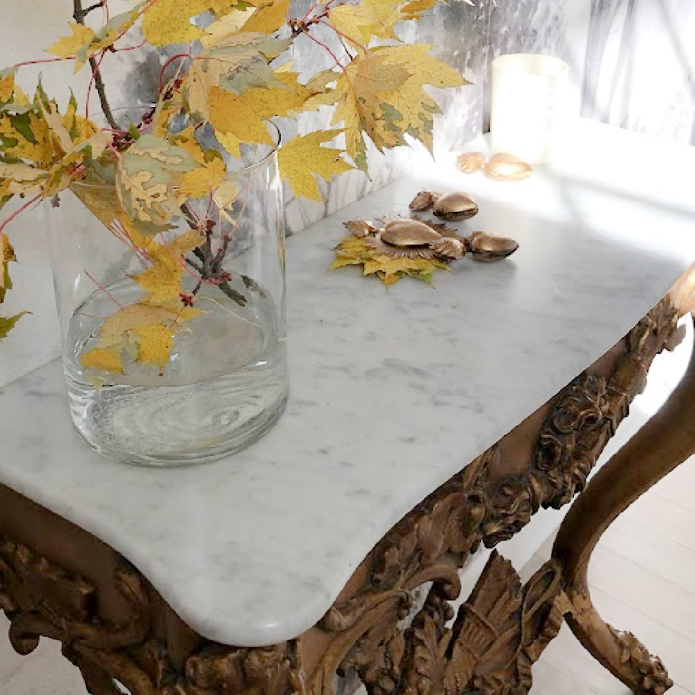 Antique French console table with marble top in my entry (wall has grisaille mural) with fall leaves in vase and gold milagro heart boxes - Hello Lovely Studio.