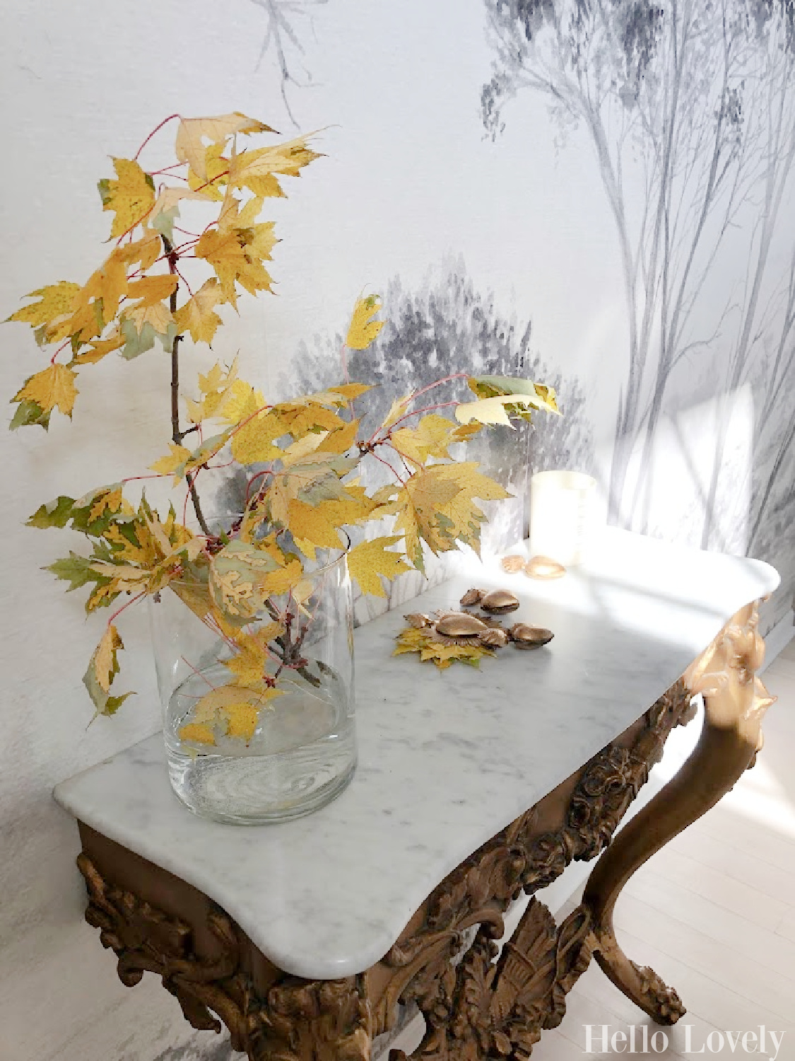 Antique French console table with marble top in my entry (wall has grisaille mural) with fall leaves in vase and gold milagro heart boxes - Hello Lovely Studio.