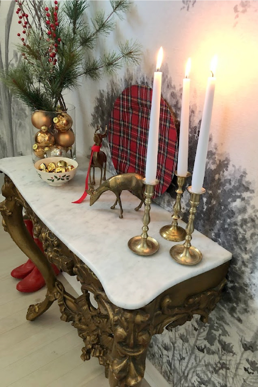 Brass candlesticks, vintage deer, and a Lenox holiday bone china bowl on a console table in our entry with scenic wallpaper mural - Hello Lovely Studio.