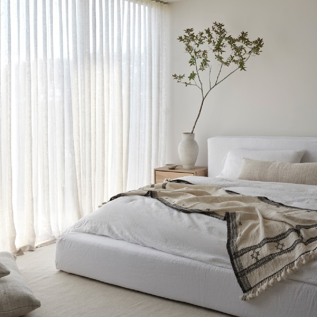 Minimal luxe neutral bedroom with white linen upholstered low bed and organic branch in vase - Michael Del Piero designed.