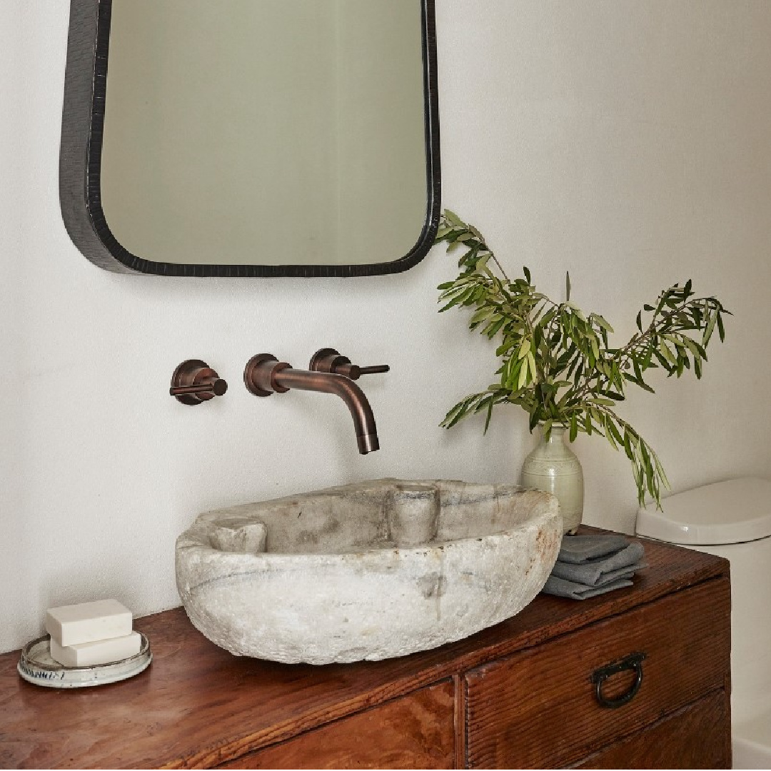 Michael Del Piero designed modern rustic luxe bathroom with stone sink, wall mount faucet, and repurposed chest.