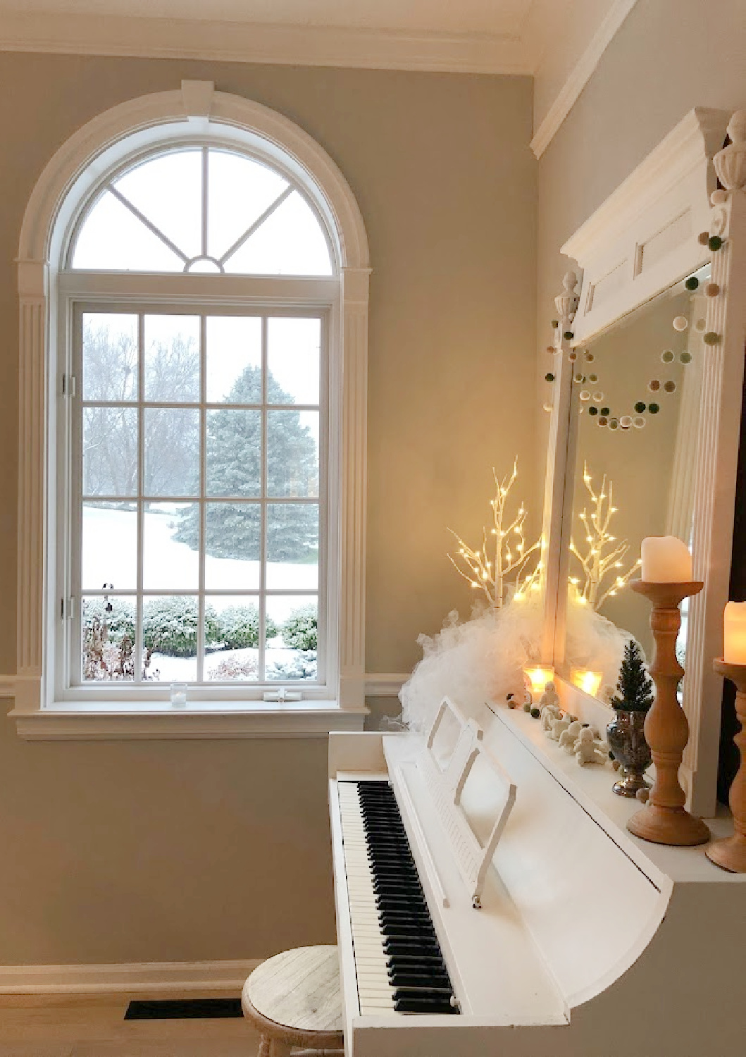 My vintage white piano decorated for Christmas and snow outside the arched window in the music room - Hello Lovely Studio.