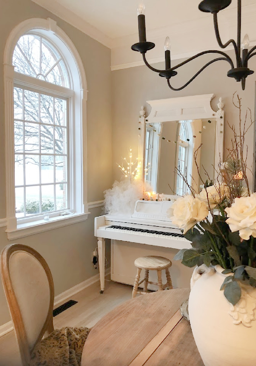 My vintage white piano decorated for Christmas and snow outside the arched window in the music room - Hello Lovely Studio.