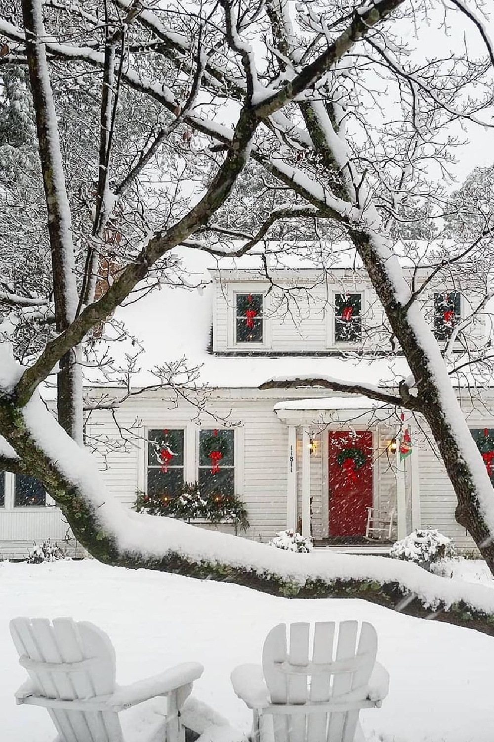 Charming red door on white house exterior decorated with wreaths for Christmas in snowy woods - Cozy Christmas on tumblr. #christmascozy