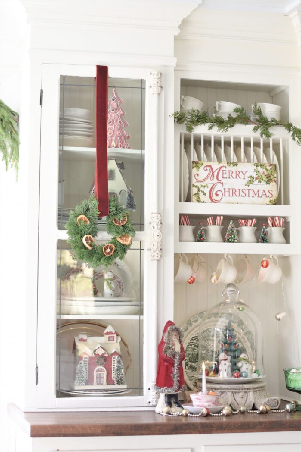 Christmas farmhouse kitchen with white cupboards and wreath with citrus slices hanging from ribbon on glass door - Follow the Yellow Brick Home. #christmaskitchen #countrychristmas #christmascitruswreath