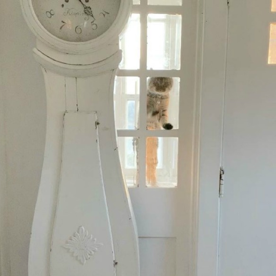 White Swedish cottage with Mora clock and cat at window - My Petite Maison. #nordicfrench #swedishcottage #swedishantiques