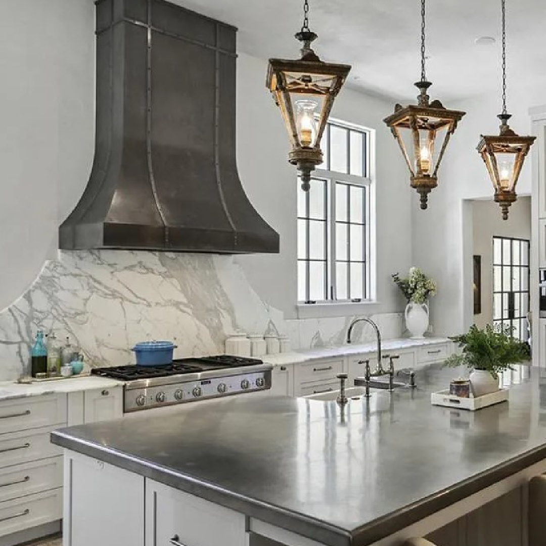 Luxurious modern French kitchen with a trio of French lanterns over island and beautiful sculptural range hood. #modernfrenchkitchen #frenchcountrykitchens