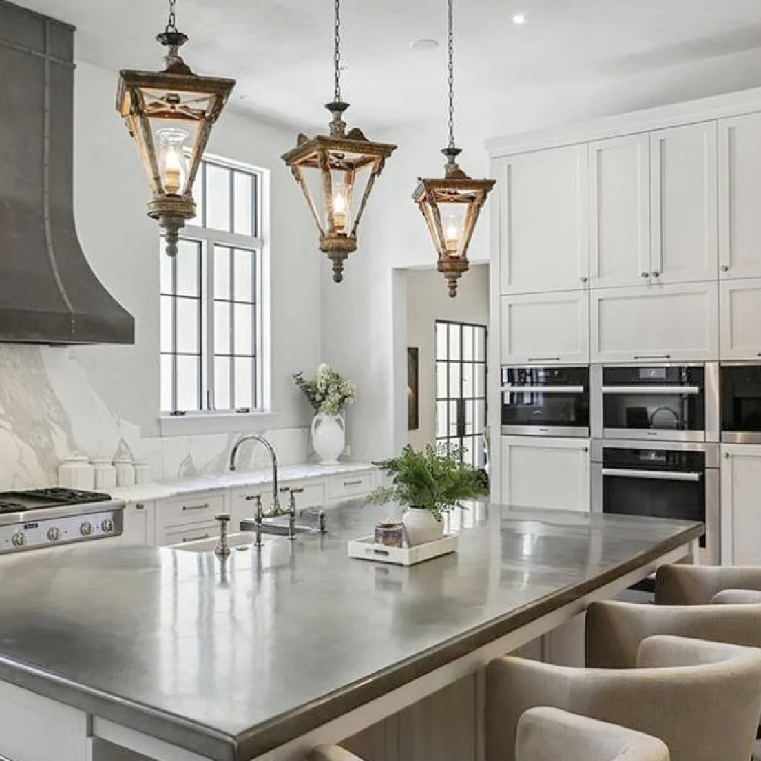 Luxurious modern French kitchen with a trio of French lanterns over island and beautiful sculptural range hood. #modernfrenchkitchen #frenchcountrykitchens