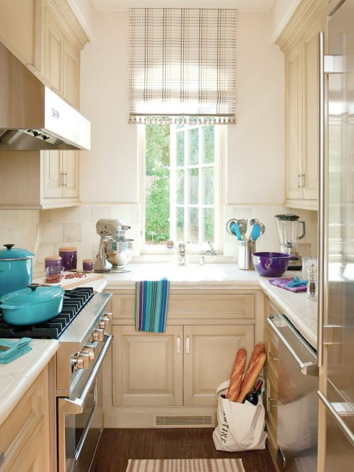 Betty Lou Phillips creates a galley kitchen with style! Neutral walls and cabinets with pops of turquoise and purple in the accessories. #tinykitchens