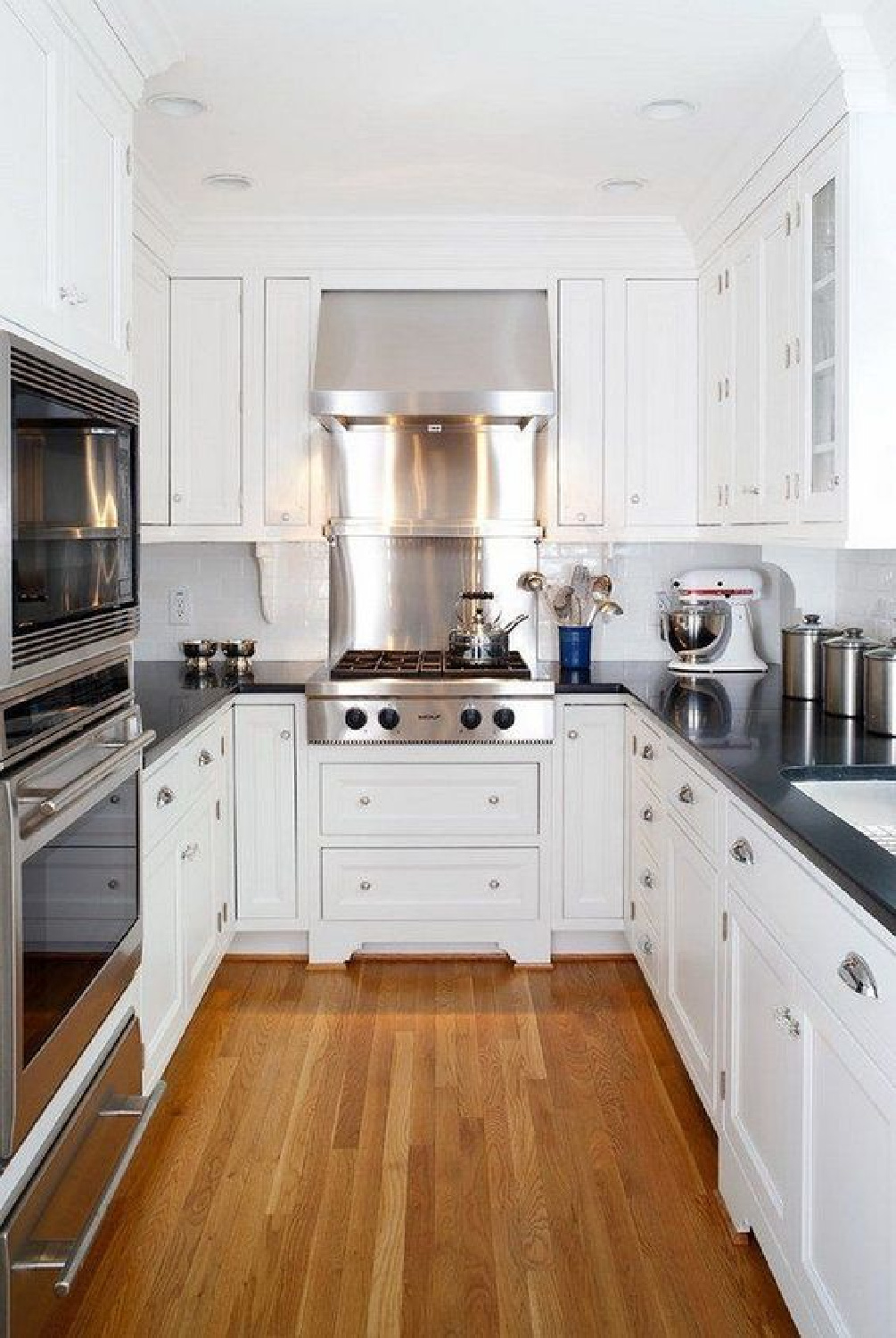 Small classic u-shaped white kitchen with black counters and wood floor - via ModernHouseMagz. #cottagekitchen #smallkitchen #ushape #kitchendesign