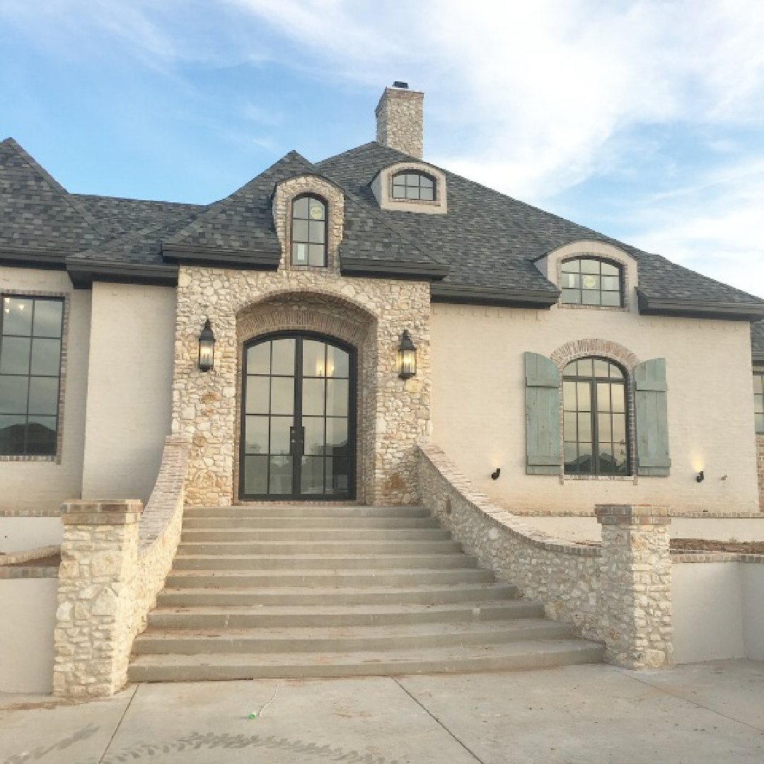 French country home exterior with arches, rustic shutters, brick, stone, and stucco. Brit Jones Design.