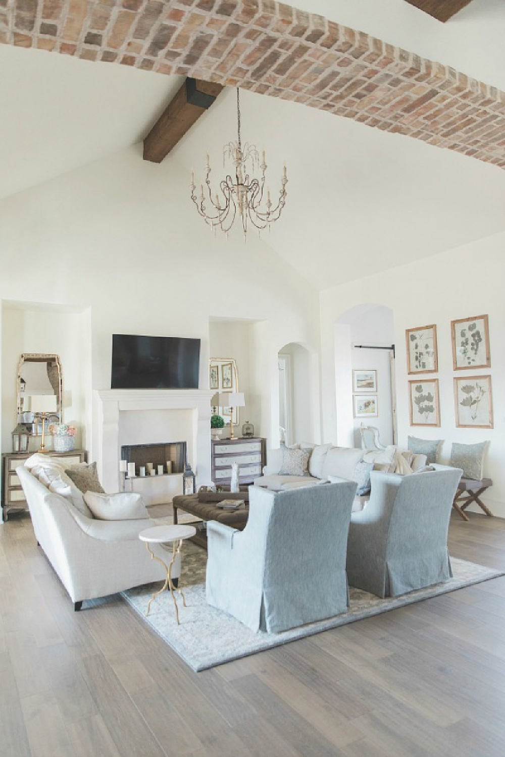 Sherwin Williams Alabaster paint color in elegant French country great room with cathedral ceiling, beams, fireplace, and French chandelier. Brit Jones Design.
