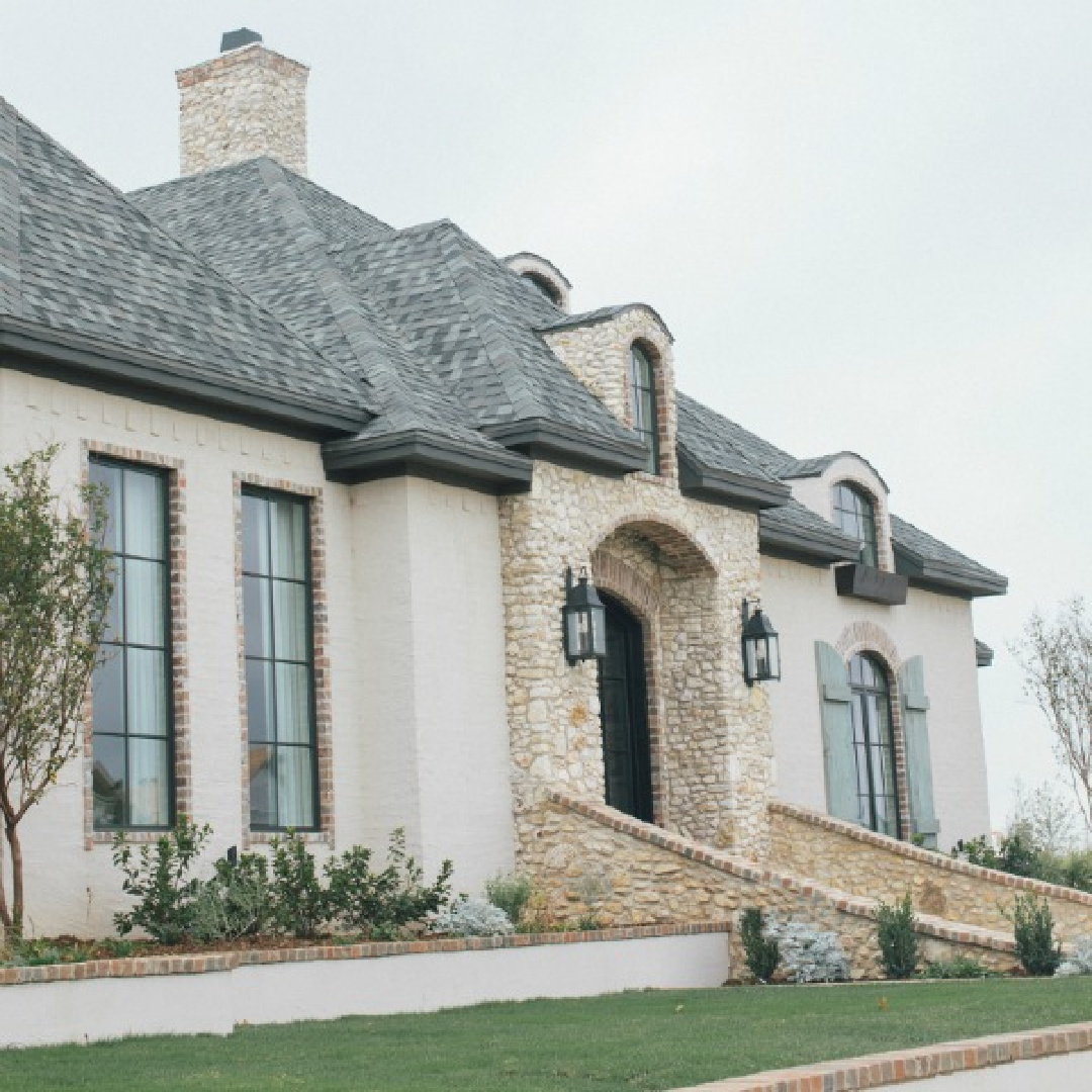 French country home exterior with arches, rustic shutters, brick, stone, and stucco. Brit Jones Design.