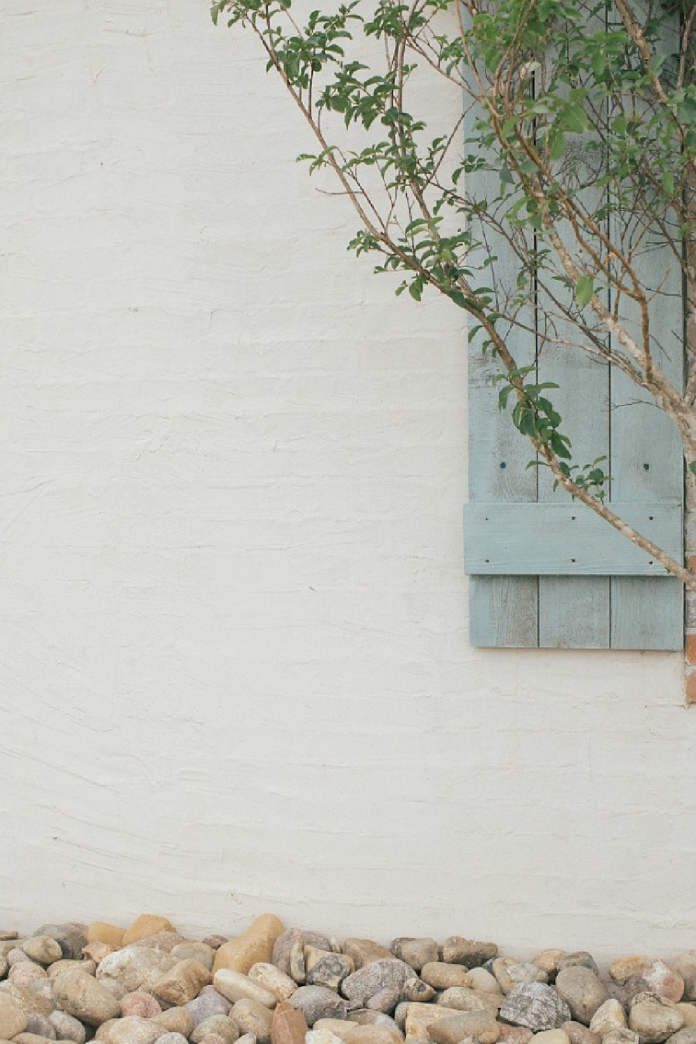 Detail of white exterior brick slurry with stucco over brick and rustic light blue shutters. Brit Jones Design.