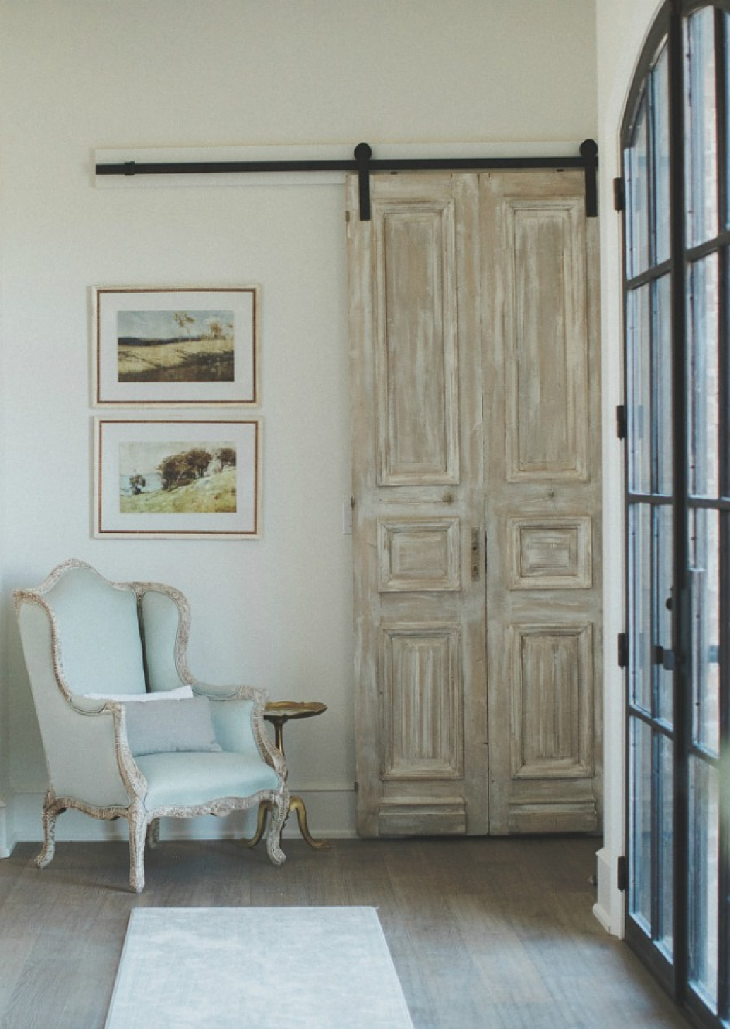 French country farmhouse entry with rustic barn door, wingback chair, steel windows, chandelier and wall sconces. Brit Jones Design.