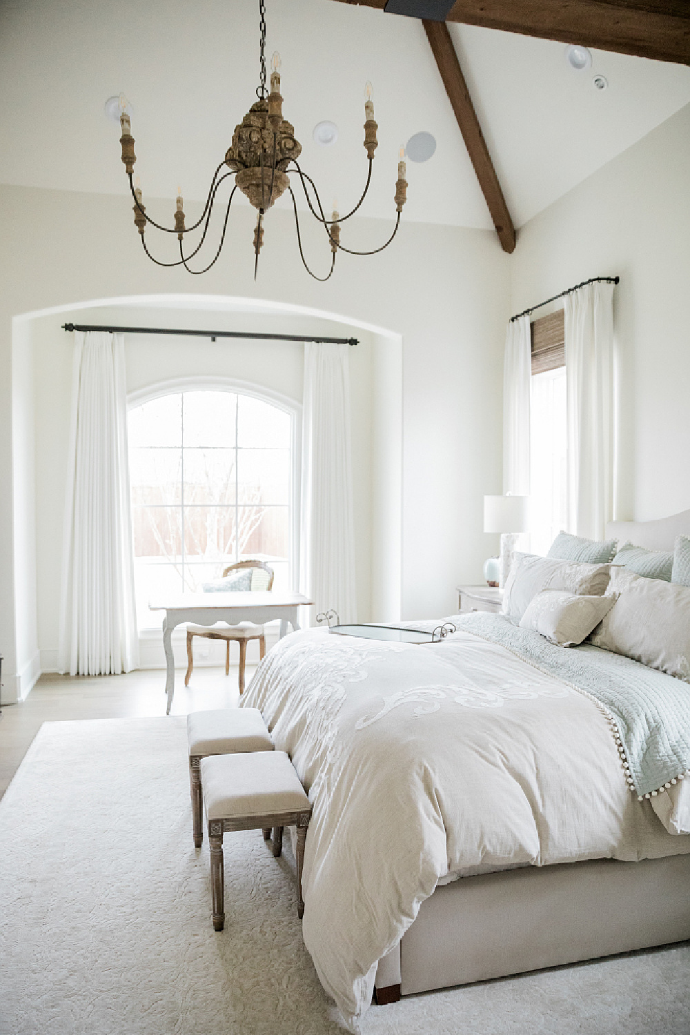 Airy, lofty, and elegant French country farmhouse bedroom with arches, desk, and bench. Brit Jones Design.
