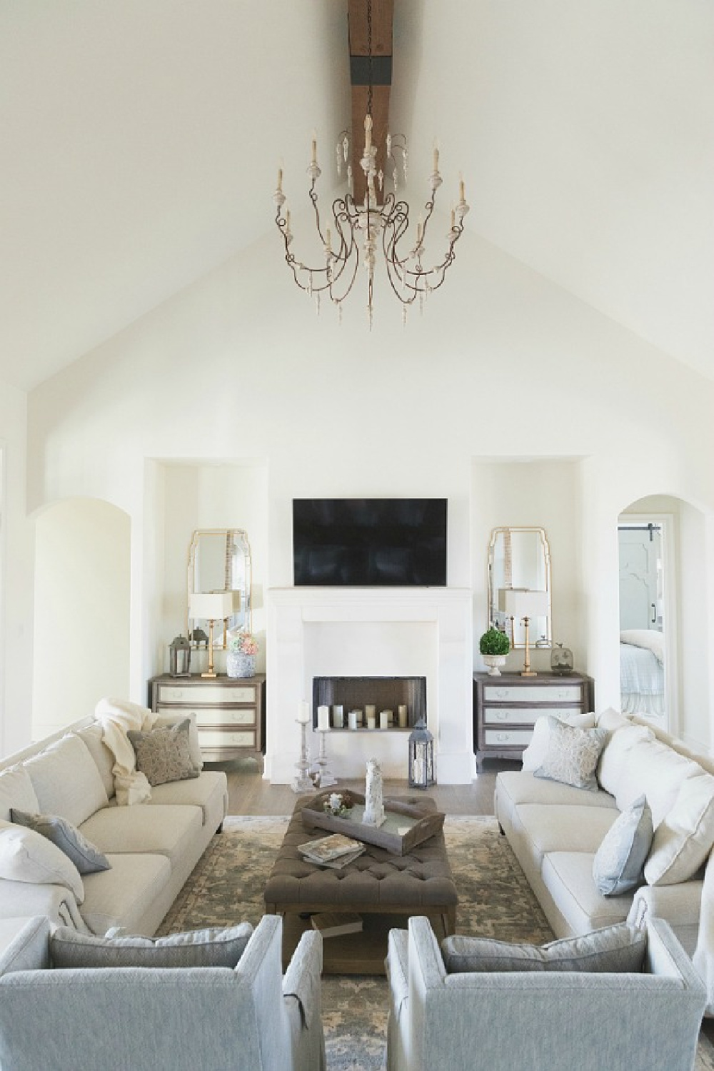 Sherwin Williams Alabaster paint color in elegant French country great room with cathedral ceiling, beams, fireplace, and French chandelier. Brit Jones Design.