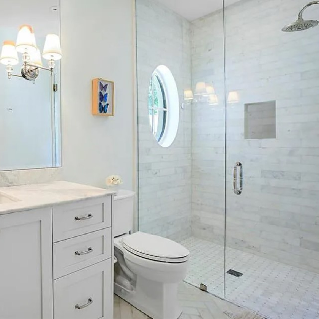 Beautiful white marble bath with oval window in shower and sconce on mirror - Atlanta luxury home on the market.