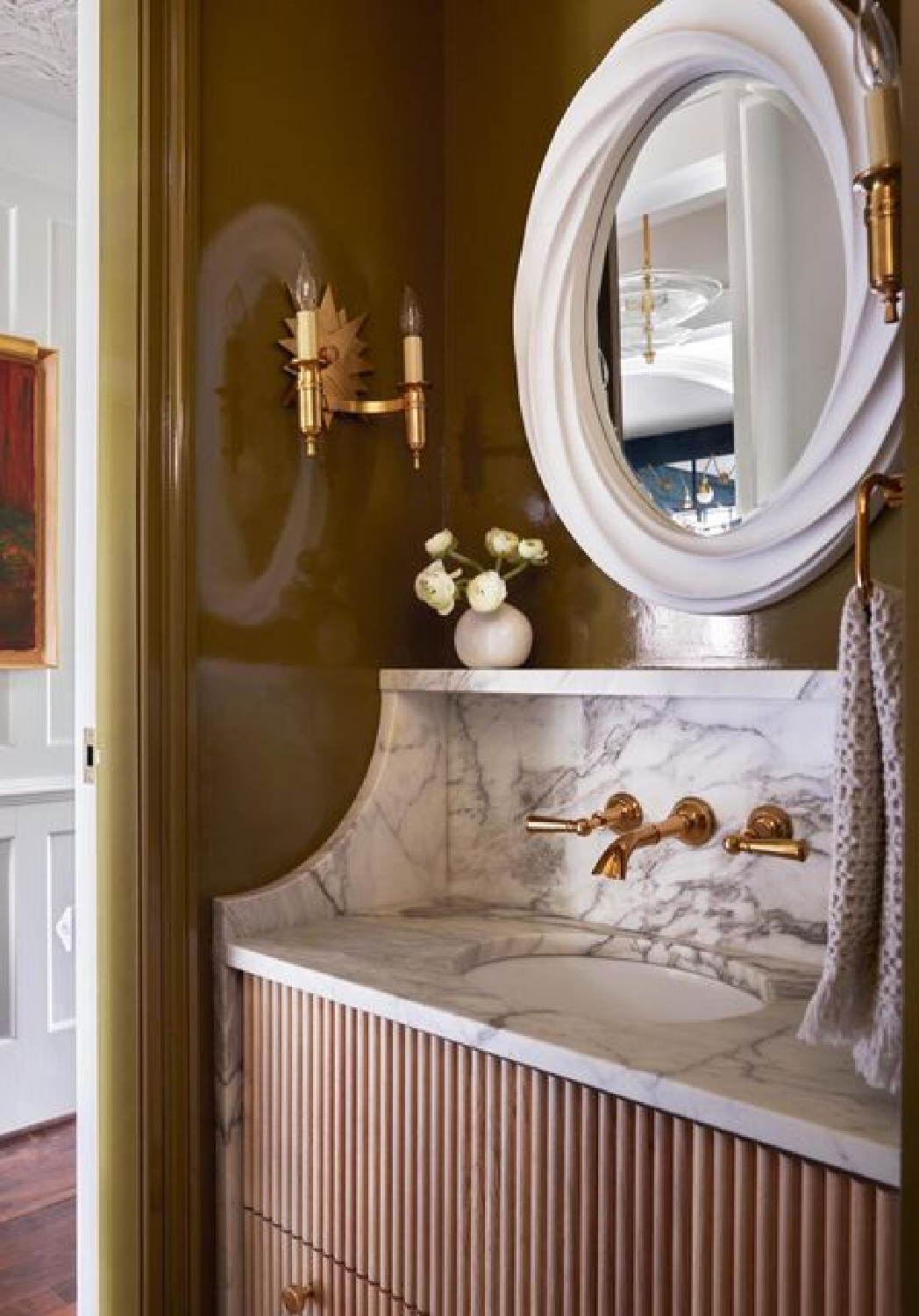 Luxurious reeded bathroom vanity, white marble backsplash with wall mount brass faucet, and double sconce.